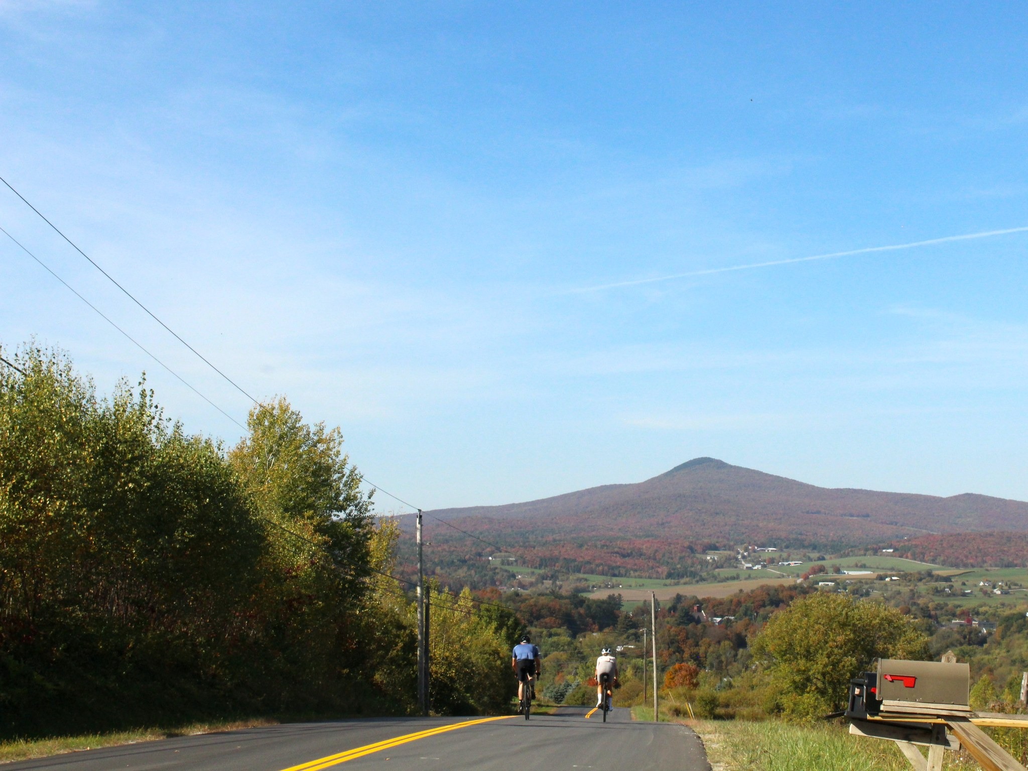 Two road cyclists descending through the autumn landscape of Northern Vermont